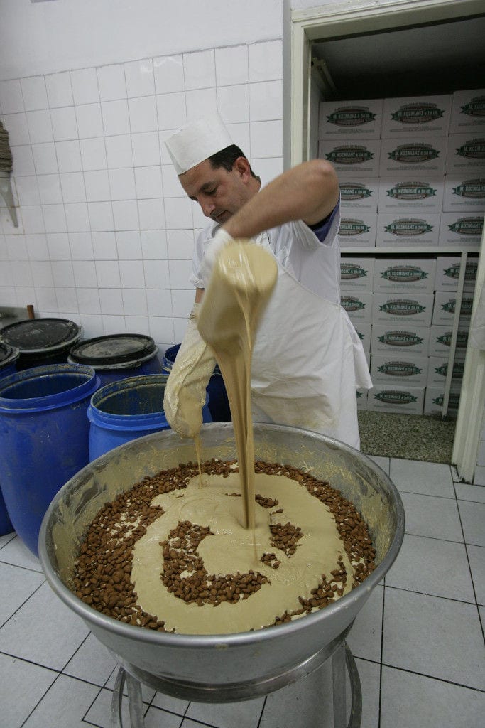 man οverturning liquid composition from decanter in a basin with almonds at 'M. Kosmidis' workshop